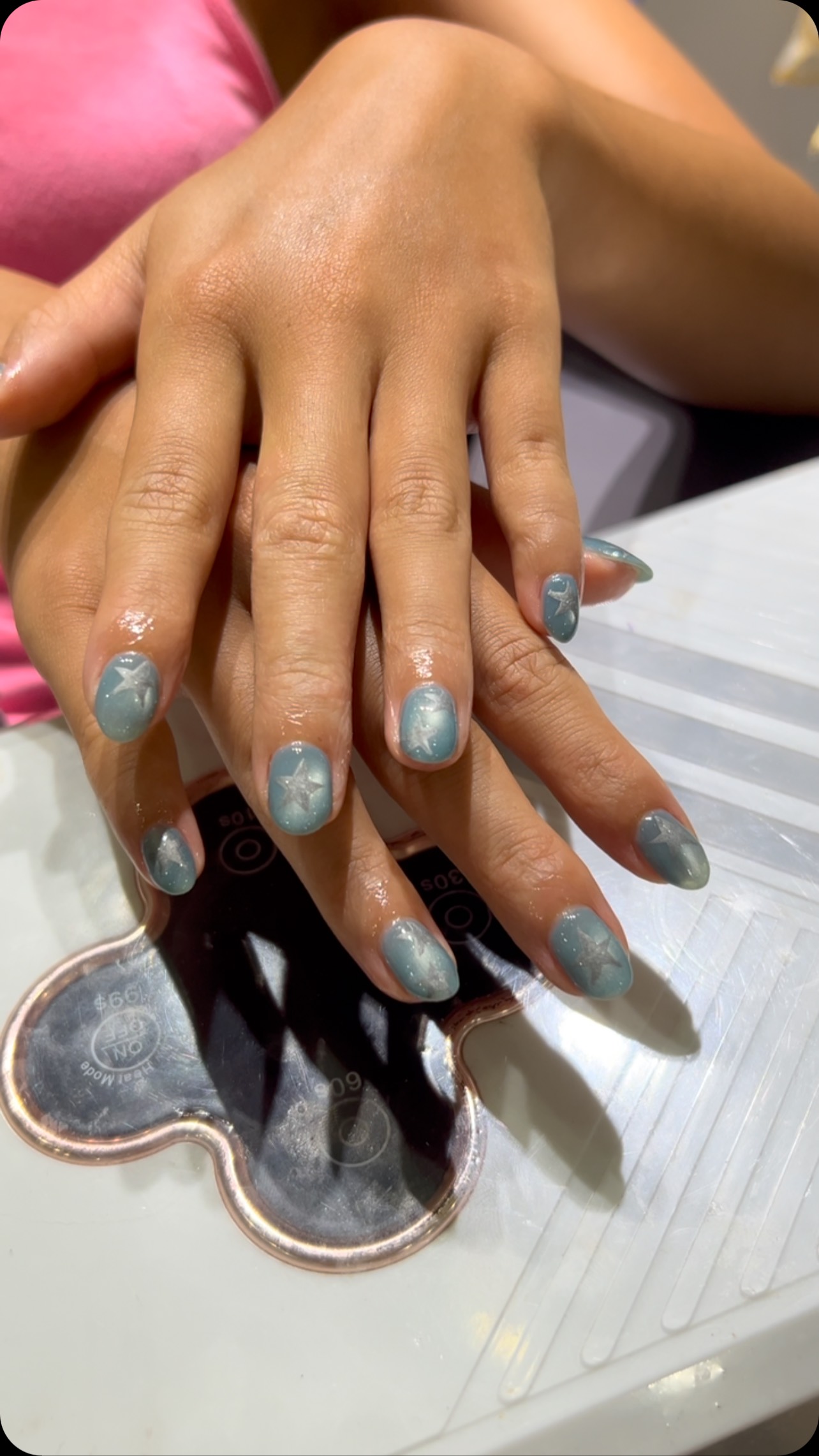 Two hands with short oval nails painted glossy light blue, each with a small star design