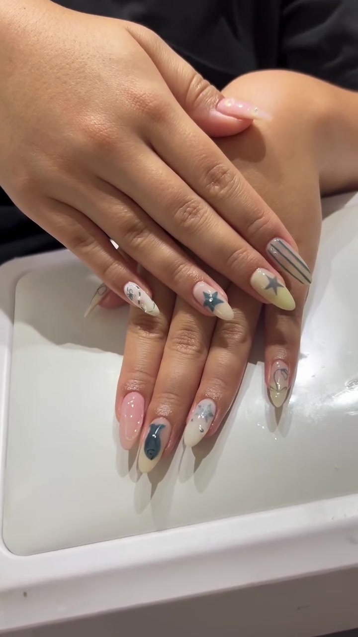 Two hands with long almond-shaped nails in a mix-and-match design of nude and pink bases with blue stars, stripes and abstract accents