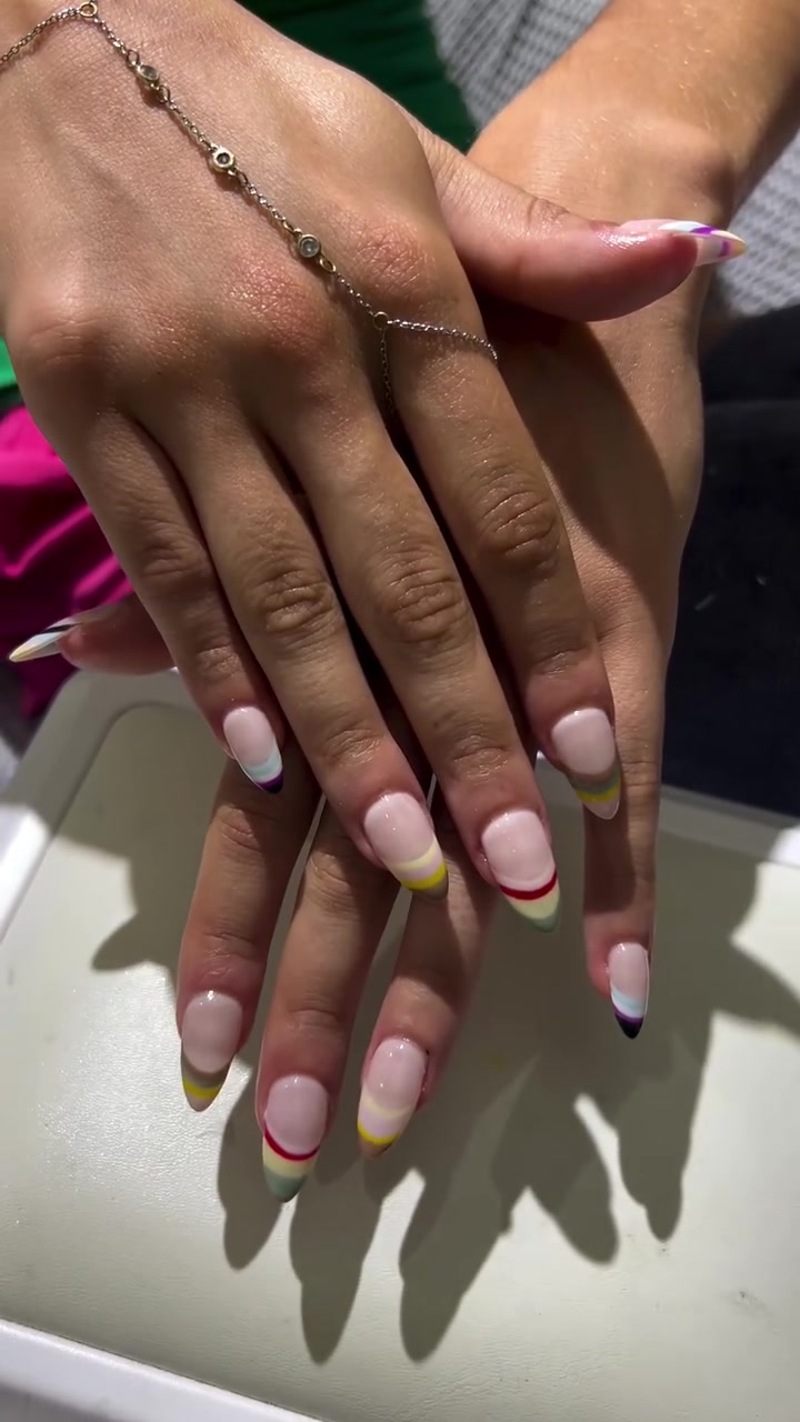 Two hands with medium square nails showing a nude base, white tips, and thin yellow, red, and purple line accents
