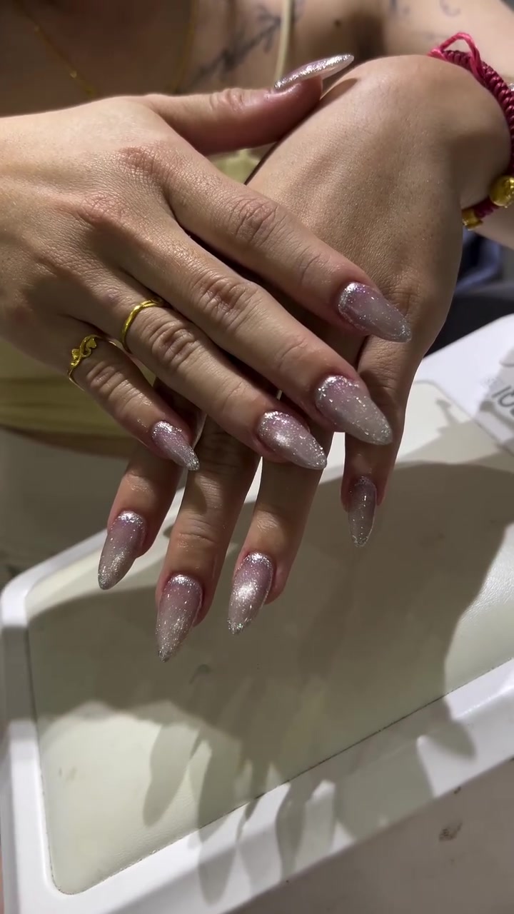 Close-up of two hands with long almond-shaped nails in a glossy pink-to-white ombre with silver glitter