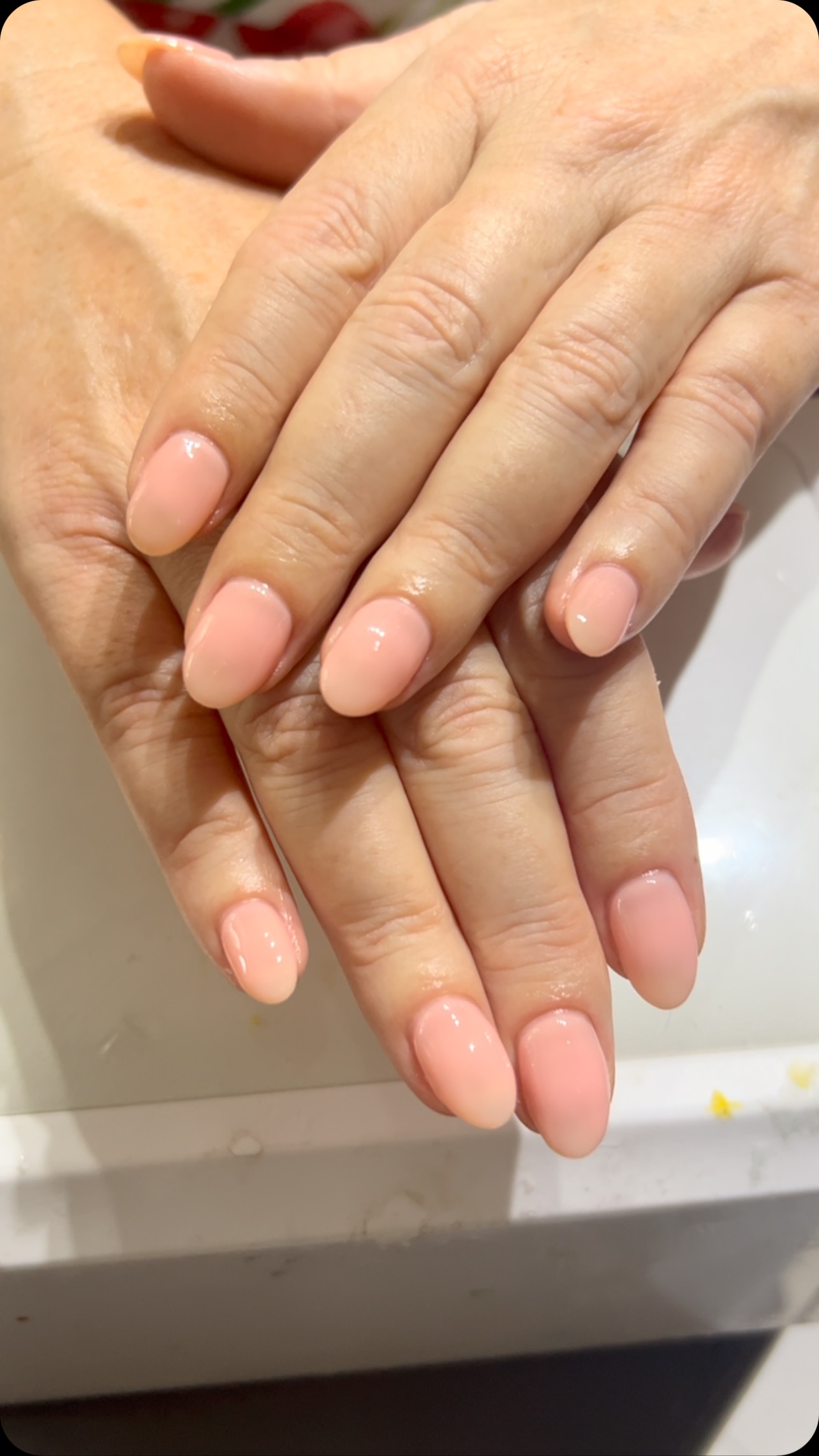 Two hands with short oval nails painted in glossy light pink-nude polish