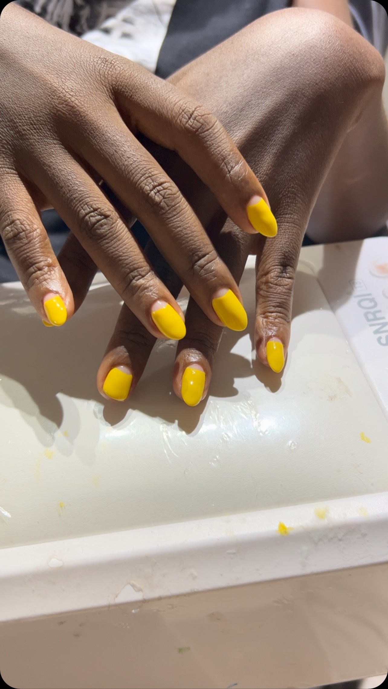 Close-up of two hands with short oval nails painted glossy bright yellow