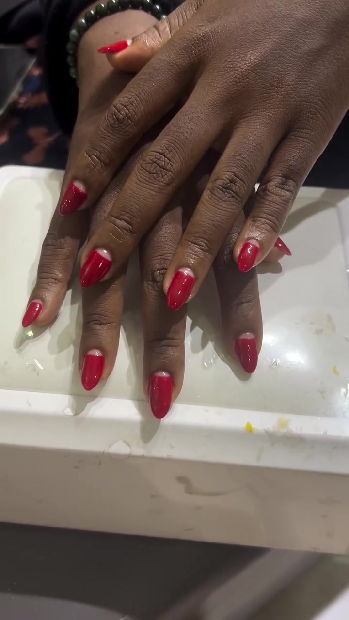Hands with medium oval nails showing a glossy red base and white French tips, resting on a white surface