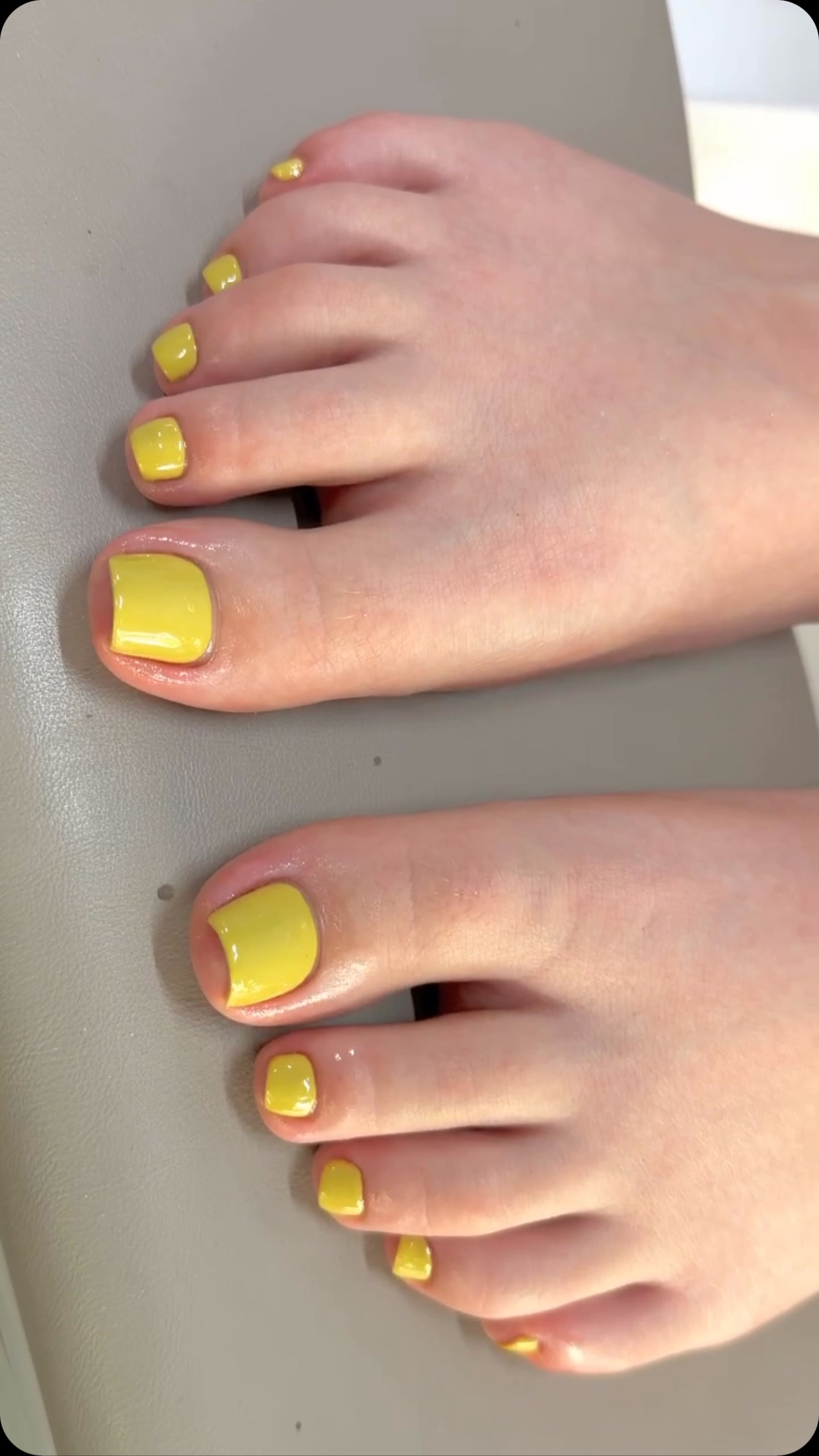 Close-up of two feet with short square toenails painted in solid glossy yellow