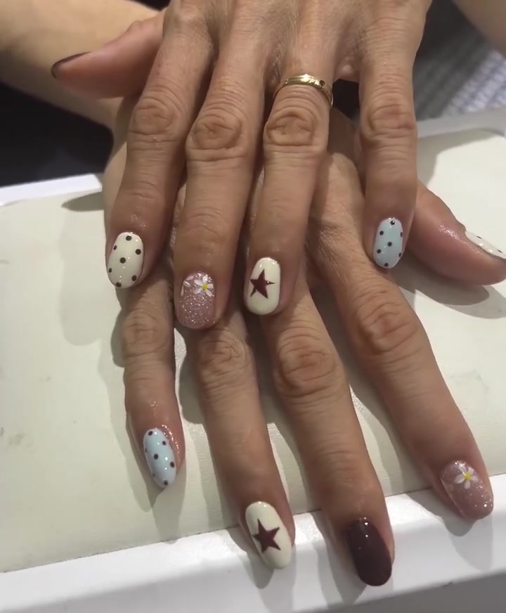 Two hands with short oval nails in mix-and-match white, blue and brown designs with polka dots, stars, floral art and glitter