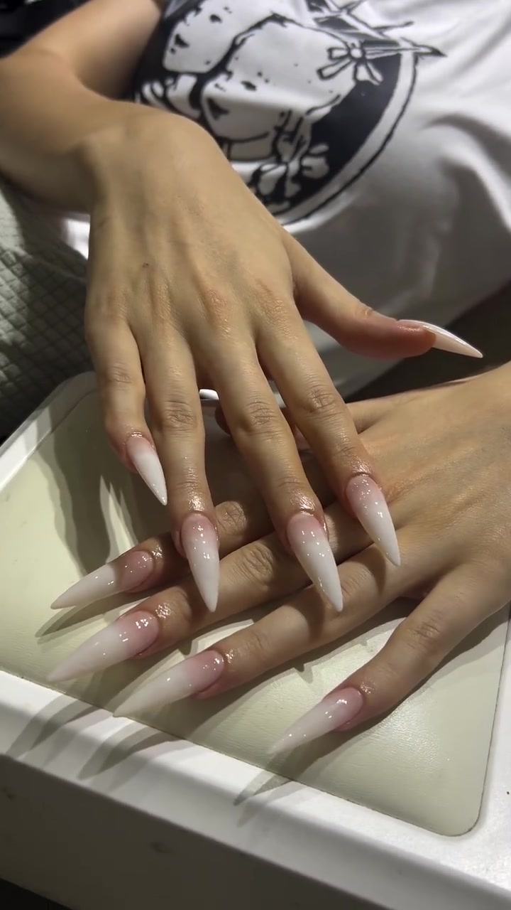 Two hands with long stiletto-shaped nails in glossy pink and white French-tip style resting on a white tray