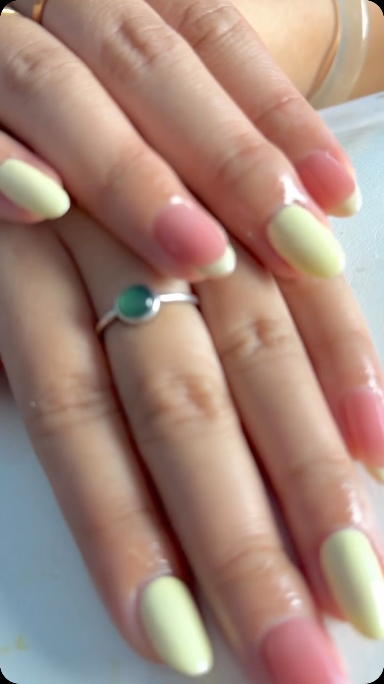 Close-up of hands with medium almond-shaped nails alternating between pink and pale yellow polish with a glossy finish